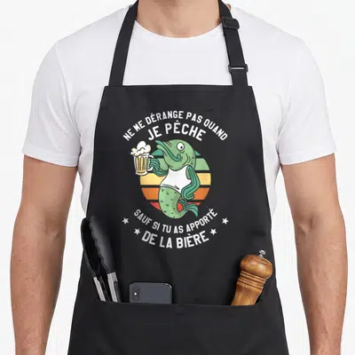 Tablier de cuisine noir avec un poisson vert tenant une bière et un texte humoristique en blanc sur fond coloré.