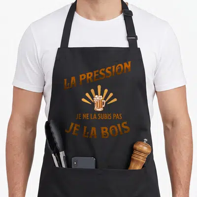 Tablier de cuisine noir avec texte La pression je ne la subis pas je la bois et illustration de verre de bière doré.