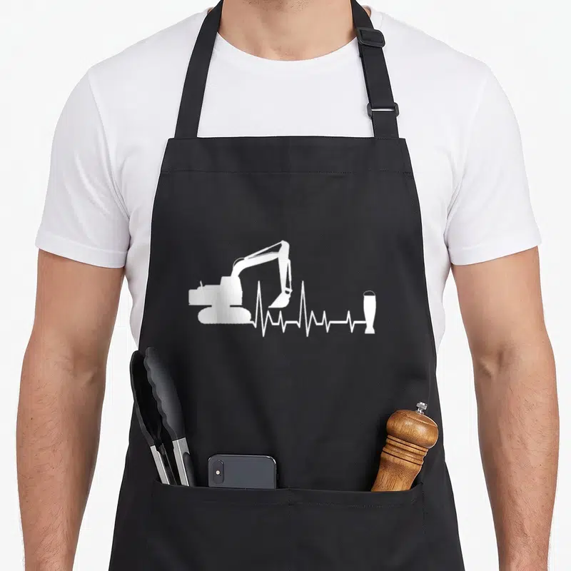 Tablier de cuisine noir avec silhouette de pelleteuse et ligne de battement de cœur se terminant par une bière.