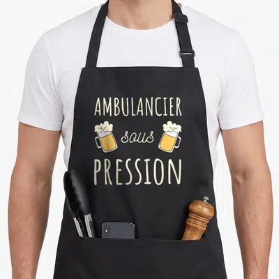 Tablier de cuisine noir avec texte ambulancier sous pression et deux verres de bière jaune à la mousse blanche.