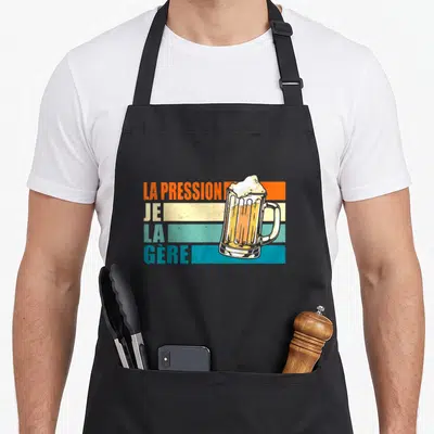 Tablier de cuisine noir avec illustration rétro d'un pichet de bière et texte La pression je la gère sur bandes colorées.