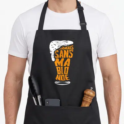 Tablier de cuisine noir avec texte orange Jamais sans ma blonde et mousse blanche en forme de verre.