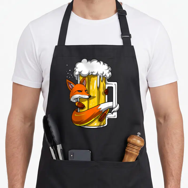 Tablier de cuisine noir avec un renard orange enlaçant une grande chope de bière à la mousse blanche.