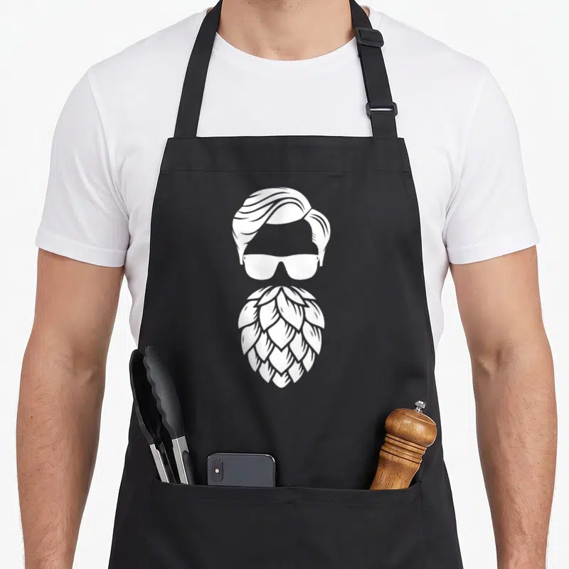 Tablier de cuisine noir avec illustration blanche d'une barbe houblon, lunettes de soleil et coiffure vintage.
