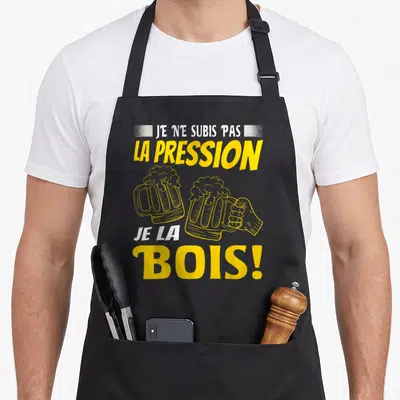 Tablier de cuisine noir avec l'inscription jaune et blanche Je ne subis pas la pression je la bois surplombant deux verres de bière.