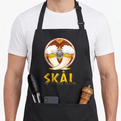 Tablier de cuisine noir avec illustration de cornes viking et linscription SKÅL en jaune.