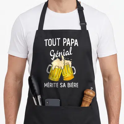 Tablier de cuisine noir avec l'illustration de deux chopes de bière et le texte Tout Papa Génial Mérite Sa Bière en blanc.