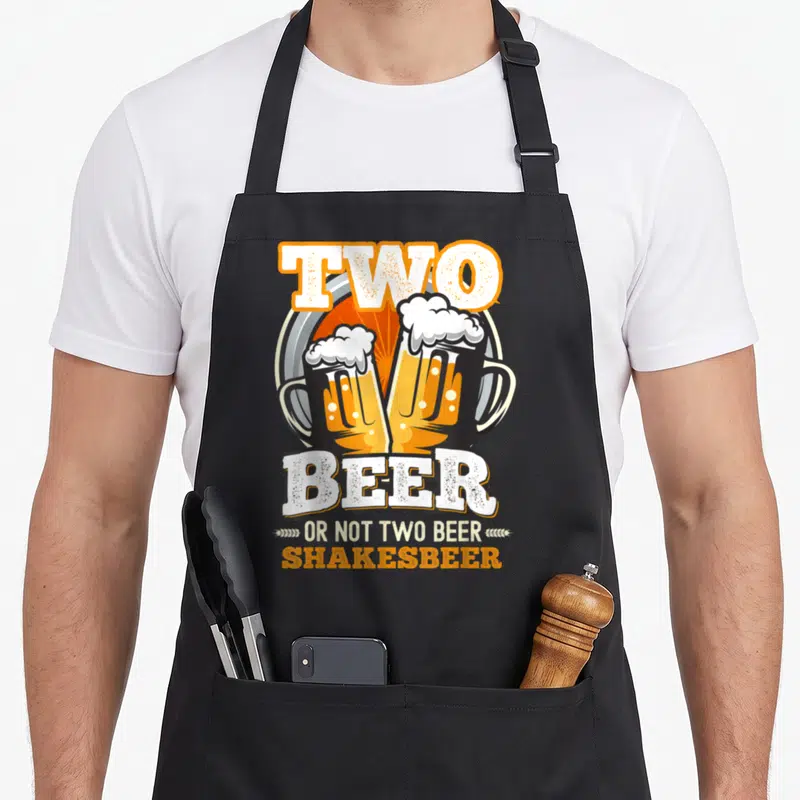 Tablier de cuisine noir avec deux verres de bière et texte Two Beer Shakesbeer imprimé en orange et blanc.