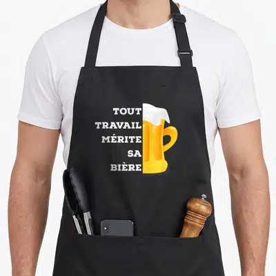 Tablier de cuisine noir avec inscription tout travail mérite sa bière et illustration de verre de bière jaune à mousse blanche.