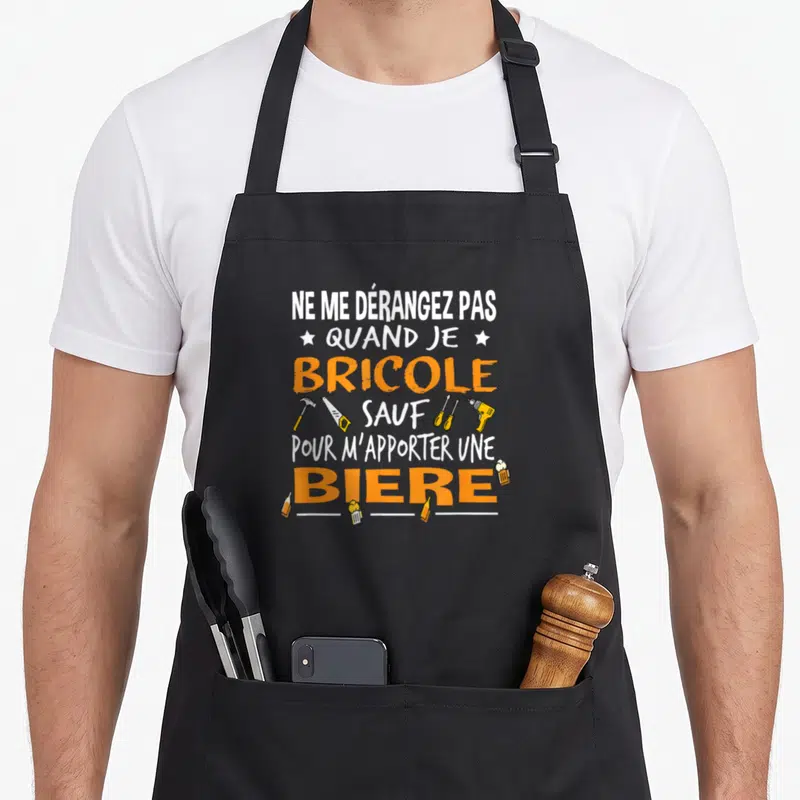 Tablier de cuisine noir avec texte blanc et orange sur le bricolage et la bière entouré d'outils dessinés.