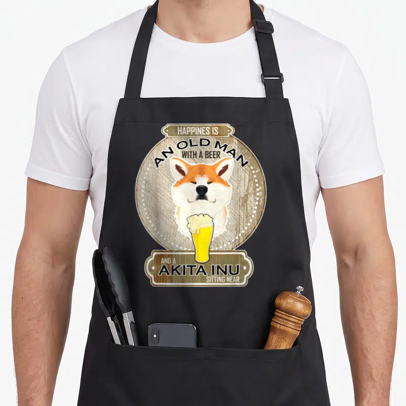 Tablier de cuisine noir avec illustration d'un Akita Inu tenant une bière et du texte anglais sur fond bois vieilli.