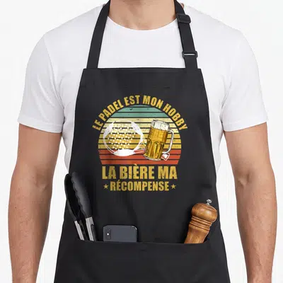 Tablier de cuisine noir avec raquette de padel et verre de bière sur fond rayé coloré retro.