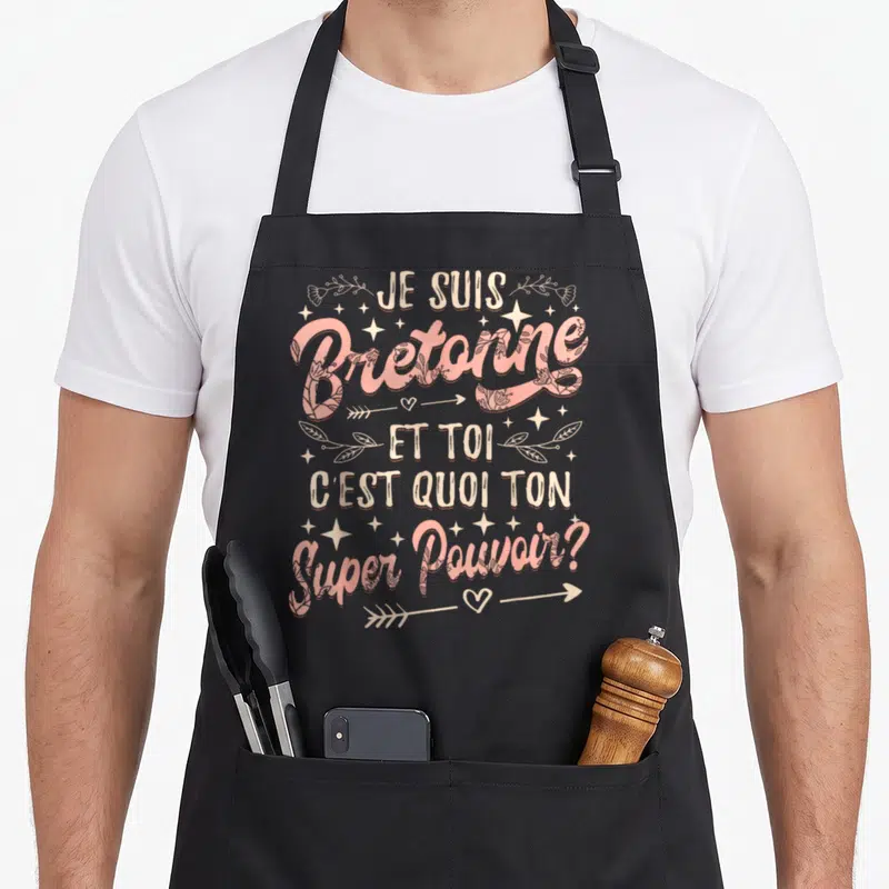 Tablier de cuisine noir avec inscription Je Suis Bretonne et Toi c'est quoi ton super pouvoir en rose et blanc entouré d'étoiles et de flèches.