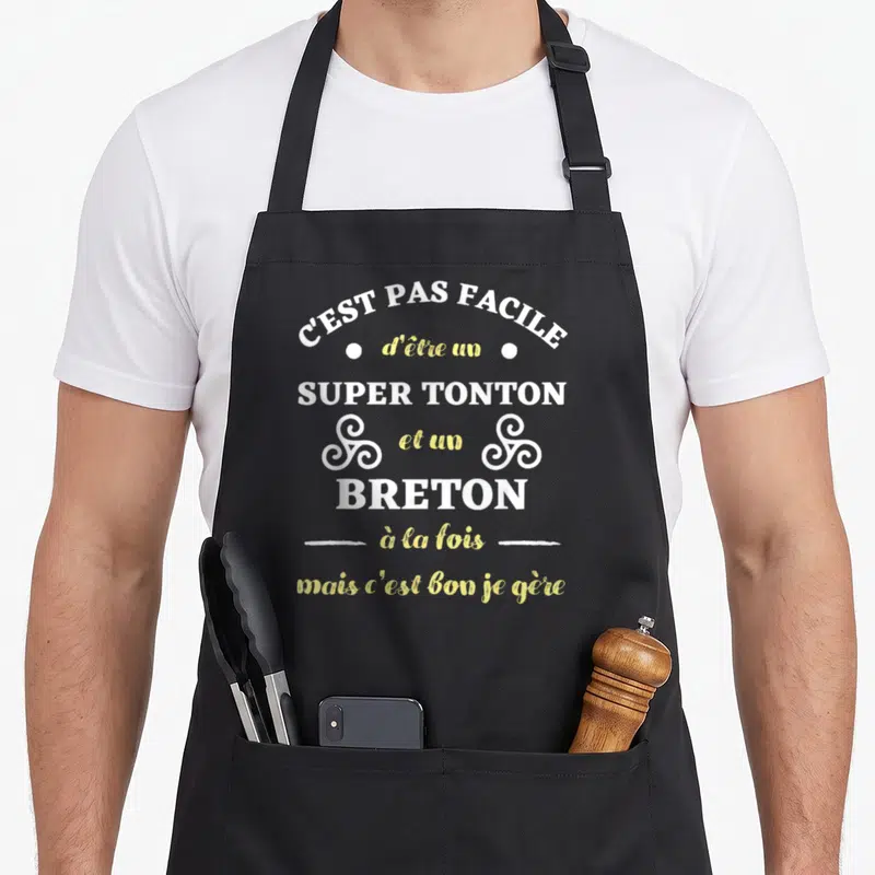 Tablier de cuisine noir avec l'inscription C'est pas facile d'être un super tonton et un breton à la fois mais c'est bon je gère en blanc et jaune.