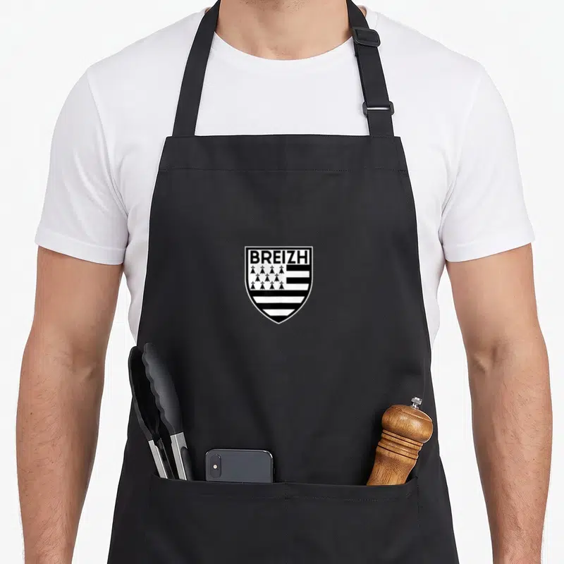 Tablier de cuisine noir avec Blason Breizh blanc et drapeau breton stylisé au centre.