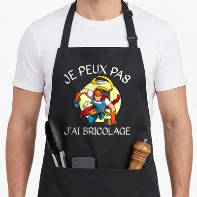 Tablier de cuisine noir avec illustration d'un ouvrier super-héros tenant une perceuse et un mètre ruban.