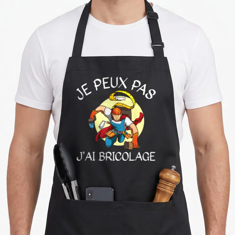 Tablier de cuisine noir avec illustration d'un ouvrier super-héros tenant une perceuse et un mètre ruban.