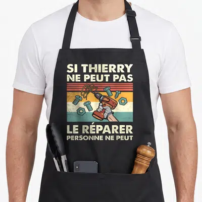 Tablier de cuisine noir avec une illustration de perceuse orange et le texte Si Thierry ne peut pas le réparer.
