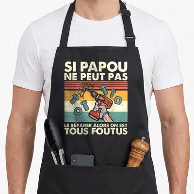 Tablier de cuisine noir avec une main tenant une perceuse orange et le texte Si papou ne peut pas le réparer alors on est tous foutus.