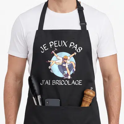 Tablier de cuisine noir avec illustration d'un bricoleur multi-bras tenant divers outils sous le texte Je peux pas j'ai bricolage.