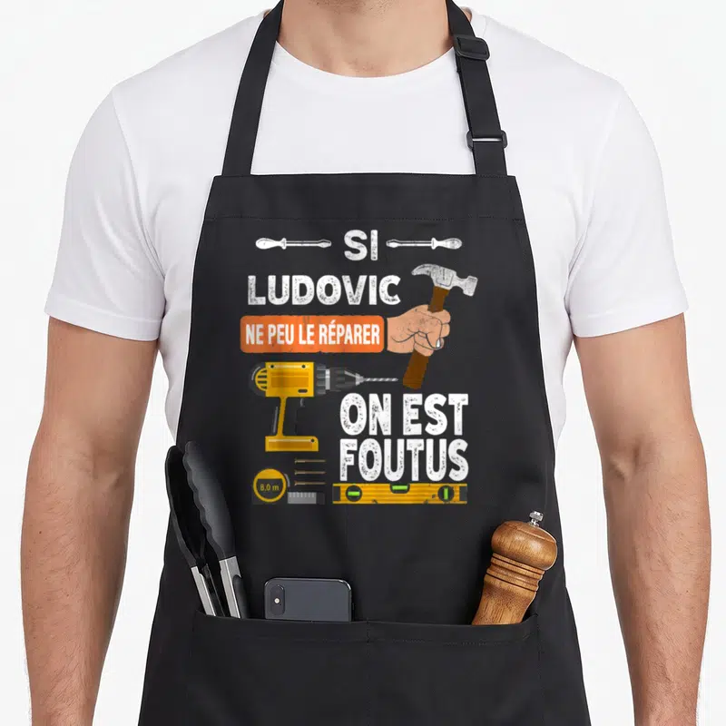 Tablier de cuisine noir avec illustration d'un marteau, perceuse jaune et texte humoristique sur fond blanc.