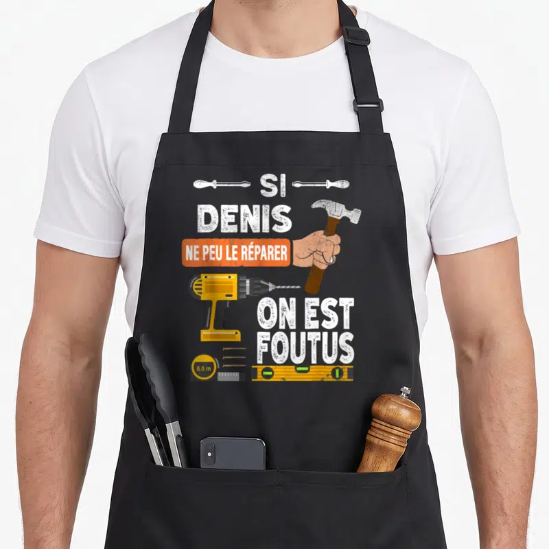Tablier de cuisine noir avec une perceuse jaune, un marteau, une level et le texte Si Denis ne peut le réparer on est foutus.