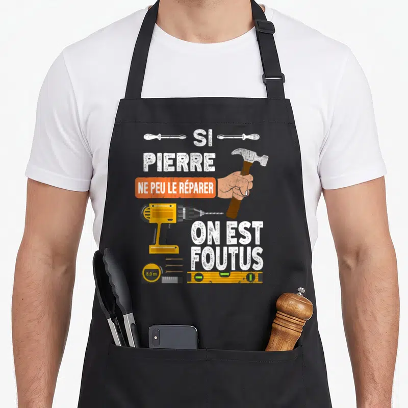 Tablier de cuisine noir avec illustration de marteau, perceuse et texte humoristique sur le bricolage.