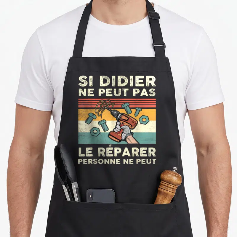 Tablier de cuisine noir avec illustration vintage d'une main tenant une perceuse et du texte humoristique sur le bricolage.