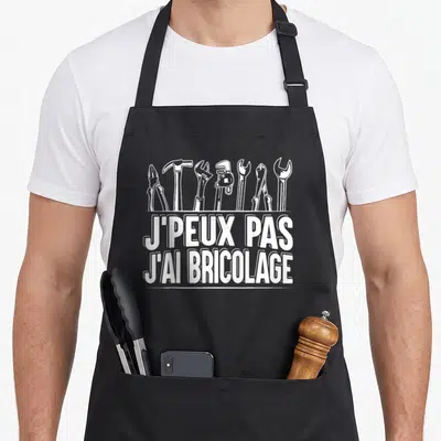 Tablier de cuisine noir avec une illustration d'outils et le texte J'peux pas j'ai bricolage en blanc.