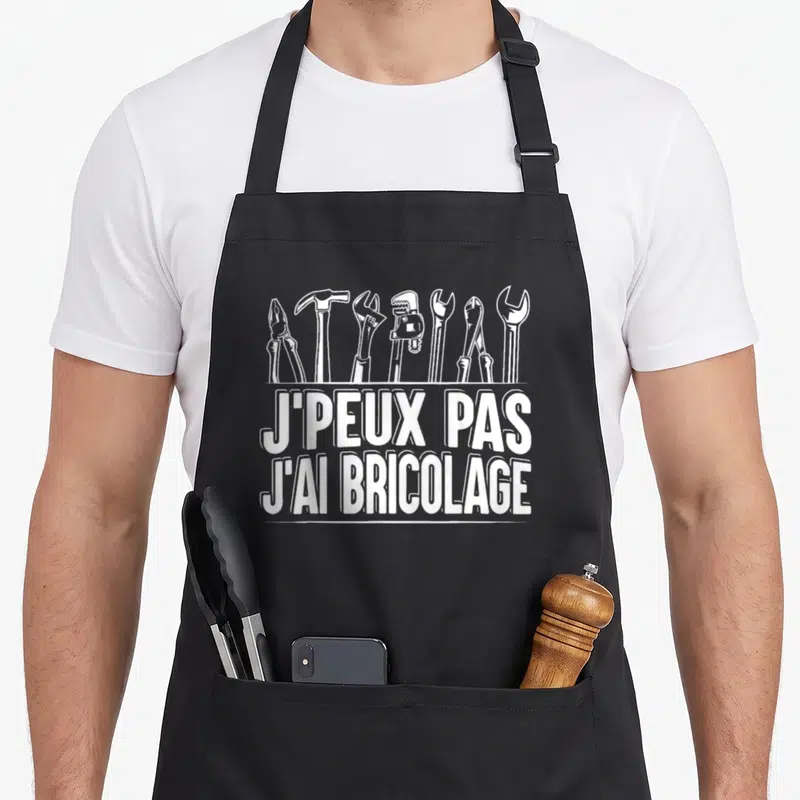 Tablier de cuisine noir avec une illustration d'outils et le texte J'peux pas j'ai bricolage en blanc.