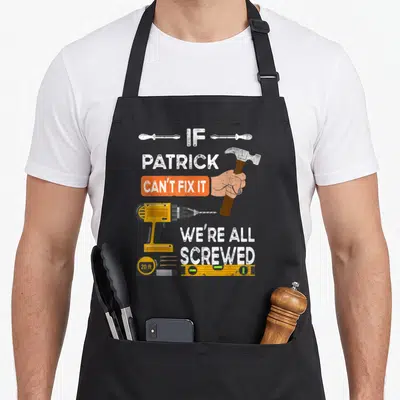 Tablier de cuisine noir avec une perceuse jaune, un marteau et le texte Si Patrick ne peut pas le réparer nous sommes tous foutus.