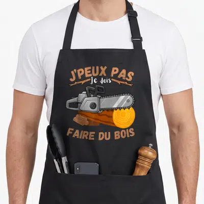 Tablier de cuisine noir avec une tronçonneuse, un tronc d'arbre et le texte J'peux pas je dois faire du bois.