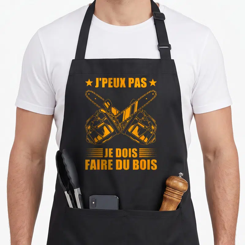 Tablier de cuisine noir avec deux tronçonneuses oranges croisées et le texte J'peux pas je dois faire du bois.