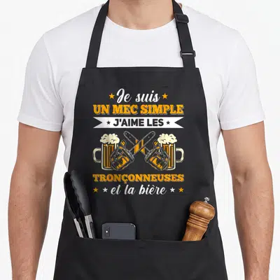 Tablier de cuisine noir avec illustration de tronçonneuses croisées et bières, texte orange et blanc.