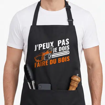 Tablier de cuisine noir avec une tronçonneuse orange et le texte J'peux pas je dois faire du bois en blanc et orange.