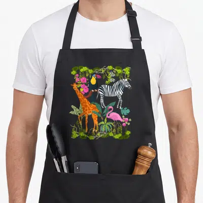 Tablier de cuisine noir avec une illustration colorée de girafe, zèbre, toucan et flamant rose au milieu de la végétation tropicale.