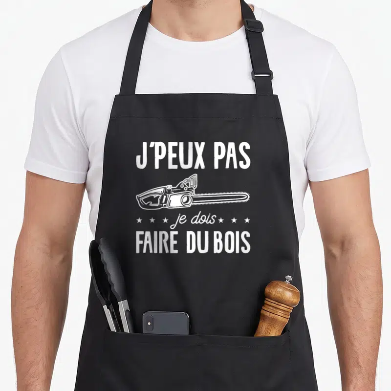 Tablier de cuisine noir avec une tronçonneuse blanche et le texte J'peux pas je dois faire du bois.