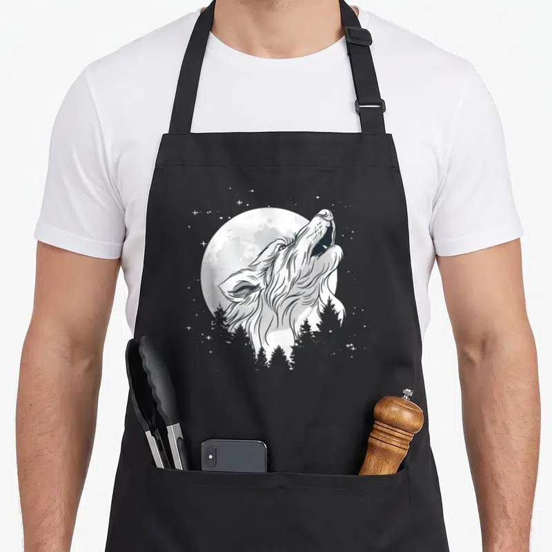 Tablier de cuisine noir avec illustration d'un loup hurlant devant une pleine lune et des arbres.