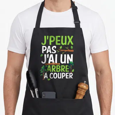 Tablier de cuisine noir avec inscription J'peux pas j'ai un arbre à couper et illustrations d'arbres verts.