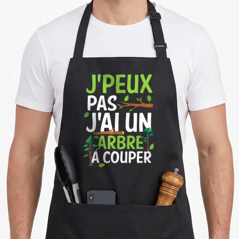 Tablier de cuisine noir avec inscription J'peux pas j'ai un arbre à couper et illustrations d'arbres verts.