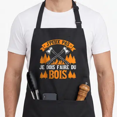 Tablier de cuisine noir avec deux haches croisées, des pins oranges et le texte Jpeux pas je dois faire du bois.