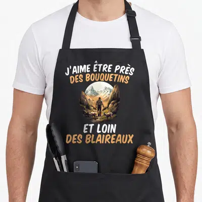 Tablier de cuisine noir avec un randonneur face à des bouquetins et une inscription humoristique sur la forêt.