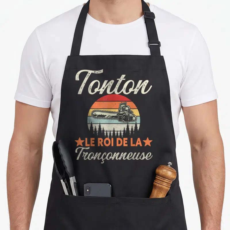 Tablier de cuisine noir avec illustration vintage Tonton roi tronçonneuse soleil et forêts.