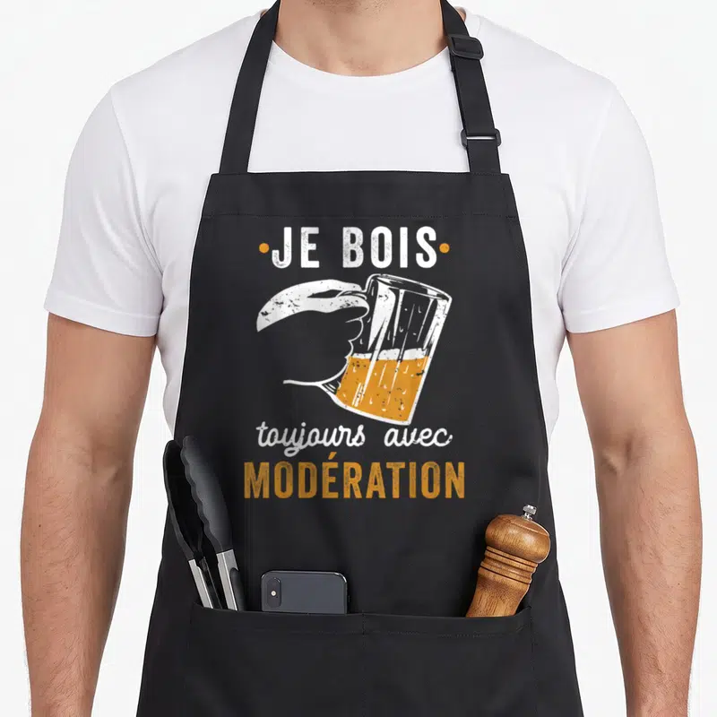 Tablier de cuisine noir avec illustration d'une main tenant une chope de bière et le texte Je bois toujours avec modération en blanc et orange.