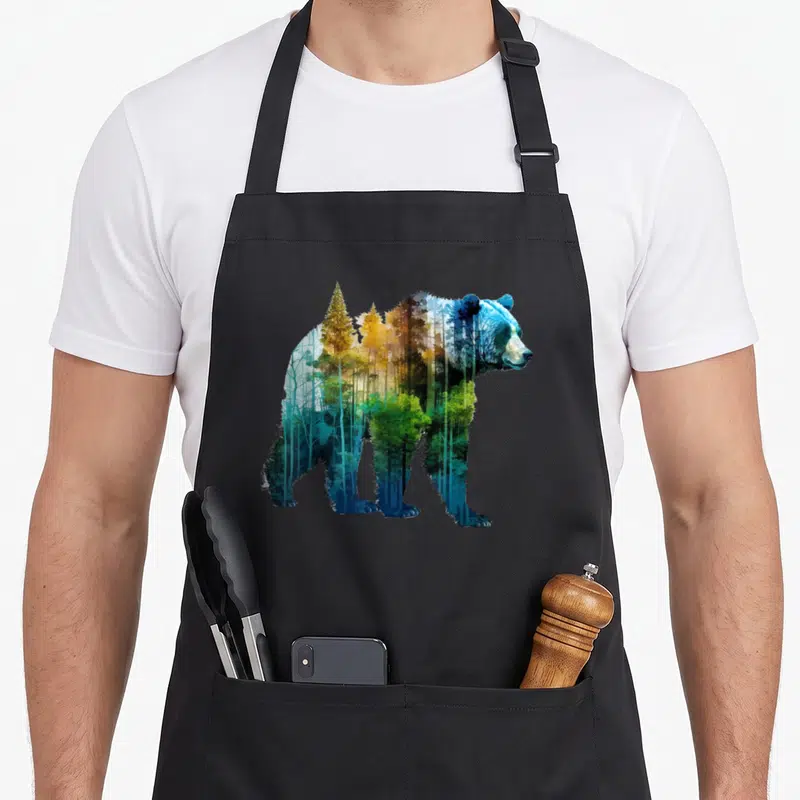 Tablier de cuisine noir avec illustration d'ours formée par une forêt aux couleurs bleu et or.