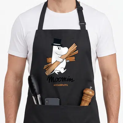 Tablier de cuisine noir avec Moominpappa blanc portant des planches de bois et un chapeau haut de forme noir.