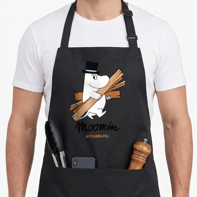 Tablier de cuisine noir avec Moominpappa blanc portant des planches de bois et un chapeau haut de forme noir.