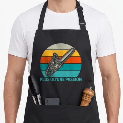 Tablier de cuisine noir avec illustration de tronçonneuse sur fond de soleil couchant coloré et texte Plus qu'une passion.