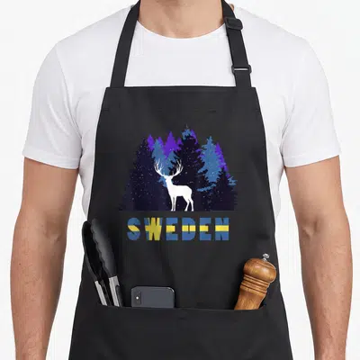 Tablier de cuisine noir avec silhouette d'orignal blanc devant une forêt bleue et le mot SWEDEN aux couleurs du drapeau.