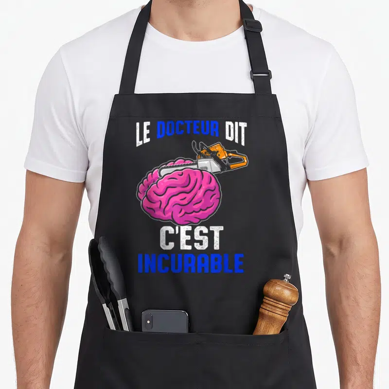 Tablier de cuisine noir avec illustration d'un cerveau rose traversé par une tronçonneuse orange et texte blanc et bleu.